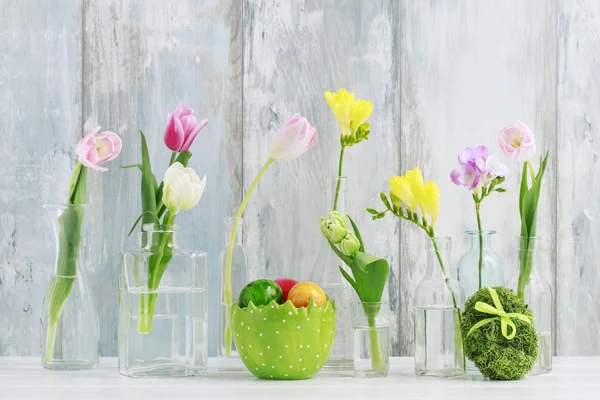 Cam şişelerde renkli çiçekler ve masadaki Paskalya yumurtaları