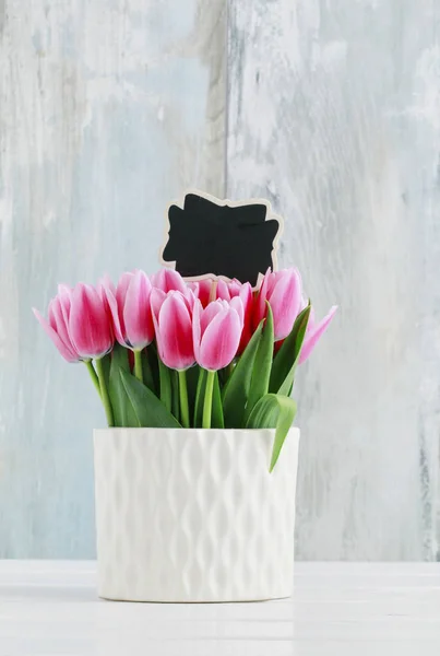 Růžové tulipány v bílé keramické váze, dřevěné pozadí. — Stock fotografie