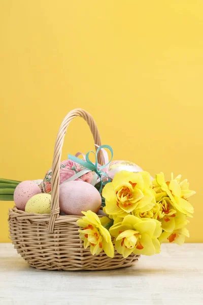 Cesta de mimbre con huevos de Pascua y ramo de flores de narciso . — Foto de Stock