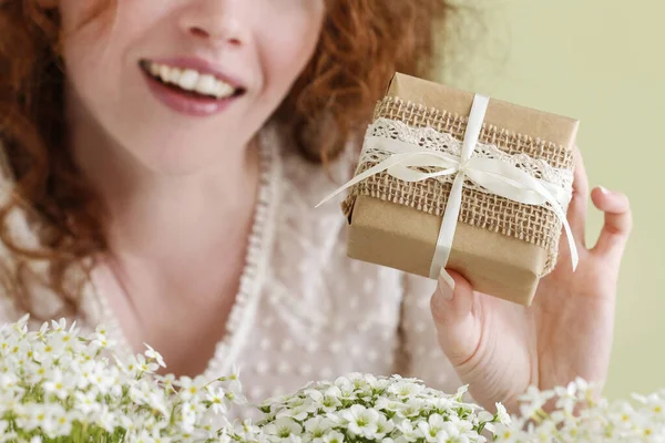 Mujer joven sostiene, un hermoso envuelto, regalo. Flores alrededor h —  Fotos de Stock