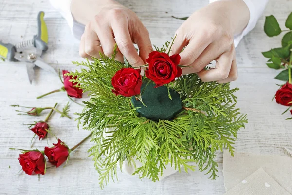 Frau zeigt, wie man ein Blumengesteck mit roten Rosen und — Stockfoto