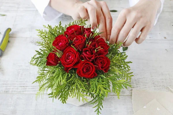 Frau zeigt, wie man ein Blumengesteck mit roten Rosen und — Stockfoto