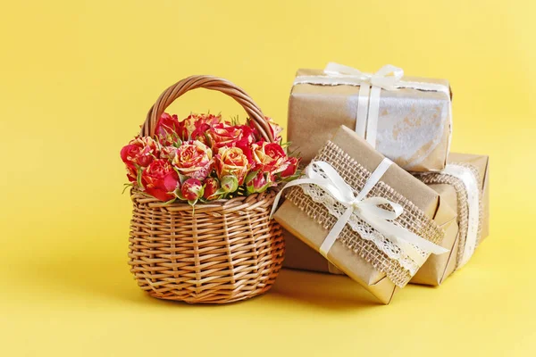 Ψάθινο καλάθι με τριαντάφυλλα και όμορφα τυλιγμένα δώρα στο κίτρινο — Φωτογραφία Αρχείου