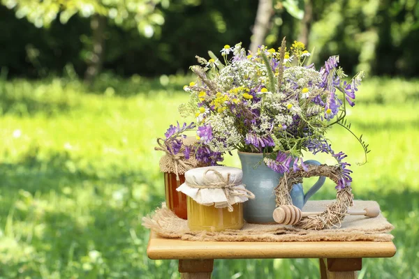 Gläser mit Honig und Strauß Wildblumen im Garten. — Stockfoto