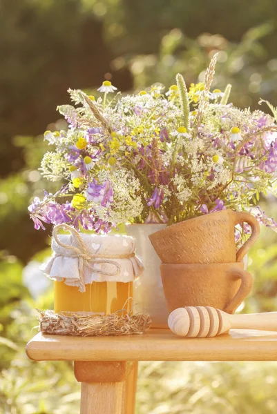 Gläser mit Honig und Strauß Wildblumen im Garten. — Stockfoto