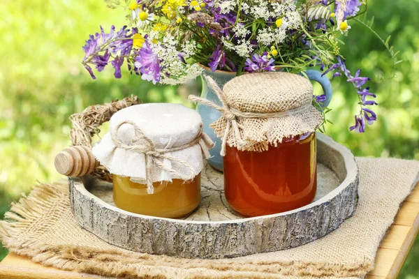 Jars with honey and bouquet of wild flowers in the garden. — Stock Photo, Image