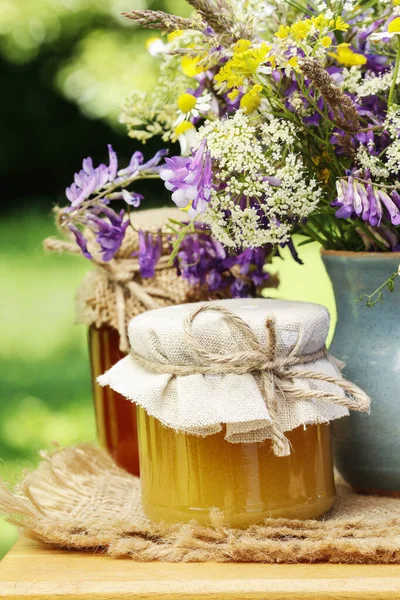 Frascos con miel y ramo de flores silvestres en el jardín . — Foto de Stock