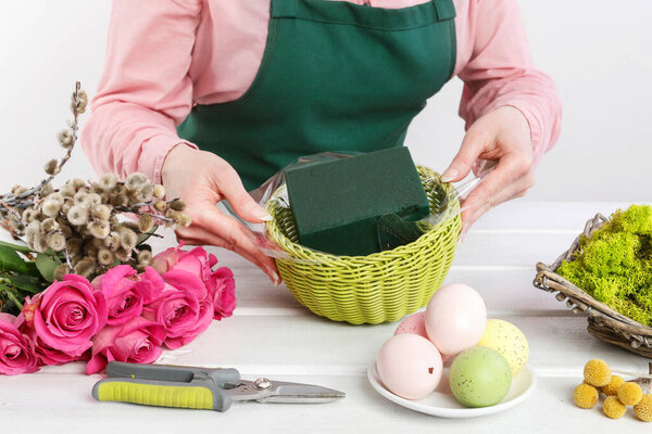 Florist at work: woman shows how to make Easter table decoration with roses, moss and catkins. Step by step, tutorial.