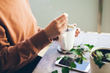 Beyaz Kupası tutarak ve aromatik infüzyonu metal çay poşeti kullanarak içmeyi çay hazırlama kadının elleri Close-up. Balkonda çay içme / Teras. Sıcak renkler, seçici odak