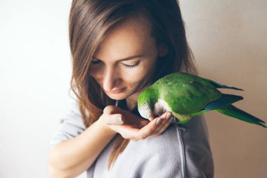 Portrait of young woman with shaming and friendly Monk parakeet parrot who is sitting on her shoulder and eating food from her hand. Film effect. Selective focus. Natural light shoot. clipart