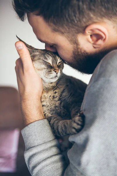 Portrait of happy cat with close eyes and beard man. Handsome young animal-lover man hugs and cuddles his tabby Devon Rex cat.