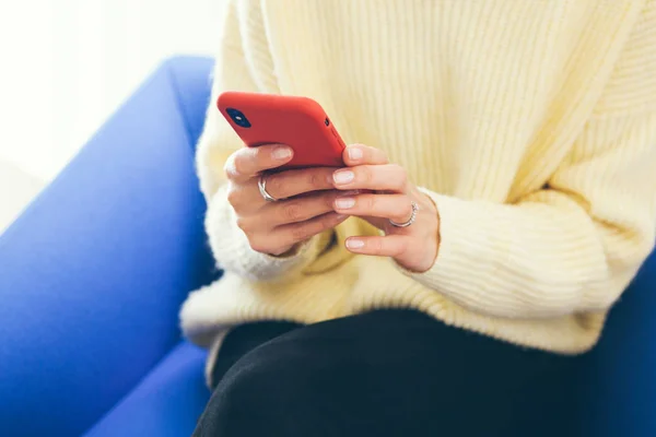 Yaşam tarzı fotoğraf. Kadın Close-Up eller holding smartphone kırmızı modern durumda ve haber okuma, sosyal ağ, web sörf / Internet smartphone içinde. Mavi koltuk arka plan.