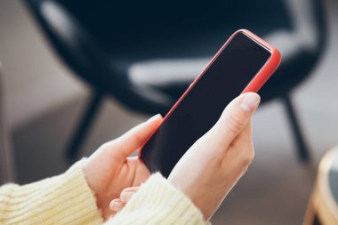 Sarı kazaklı kadın elinde akıllı telefon tutuyor, görüntüyü kapatıyor.