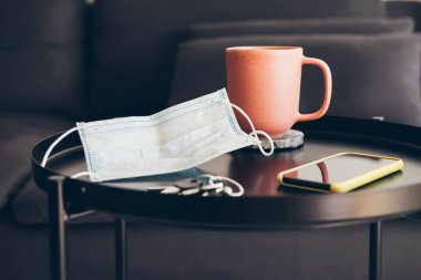 İç mekândaki sehpanın üstündeki yüz maskesini kapat. Virüsün yayılmasını önlemek için her gün yeni bir normallik. Evde güvende olmak, kendini izole etmek..