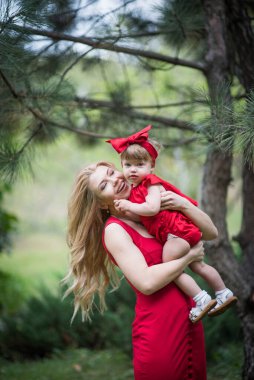 Anne ve küçük kızı sarı saçlı ve kırmızı elbiseli yeşil çimlerde kalır.