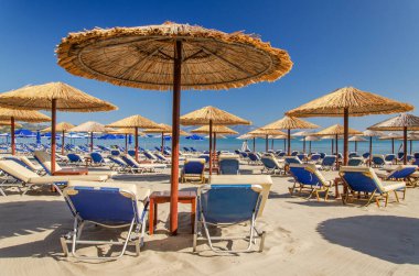 Yunanistan 'ın Zakynthos adasının doğu kıyısındaki kumlu bir sahilde saman plaj şemsiyeleri ve güneş sandalyeleri