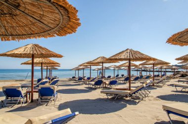 Yunanistan 'ın Zakynthos adasının doğu kıyısındaki kumlu bir sahilde saman plaj şemsiyeleri ve güneş sandalyeleri