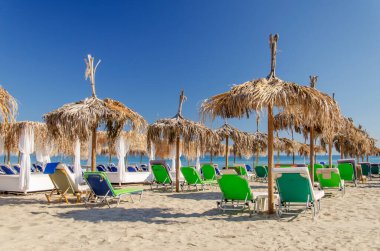 Yunanistan 'ın Zakynthos adasının doğu kıyısındaki kumlu bir sahilde saman plaj şemsiyeleri ve güneş sandalyeleri