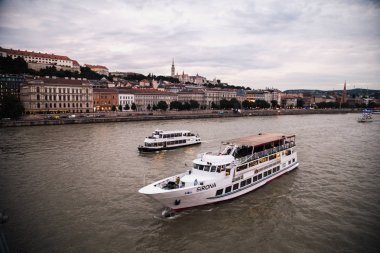 arka planda, Budapeşte geleneksel yapılar ile Dunay nehirde yüzen turistik tekneler  