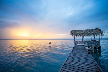 Dock with a palapa roof during sunset and calm blue water in Belize clipart