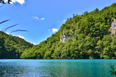 Bir lake parlak gök mavisi renginde su ile. Kaya, yeşillik içinde dalmış. Küçük bulutlar bulutlar ile yaz, mavi gökyüzü. Plitvice Gölleri, Hırvatistan.