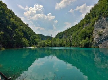 Lake parlak gök mavisi renginde su ile. Kaya, yeşillik içinde dalmış. Küçük bulutlar bulutlar ile yaz, mavi gökyüzü. Plitvice Gölleri, Hırvatistan.