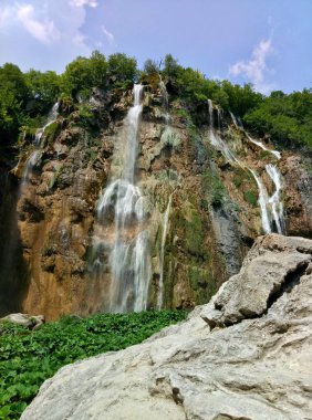 Yaz aylarında Hırvatistan Plitvice Gölleri üzerinde en yüksek 78 metre şelale. Ön planda bir kaya. Mavi gökyüzü bulutlar olmadan.