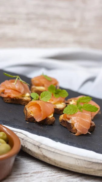 Smoked salmon toast with mint leaf on black stone and old wooden board with space for your text - image