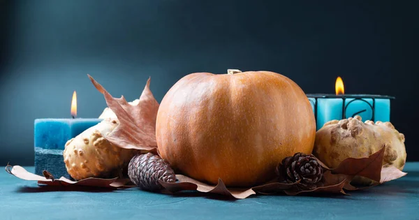 Calabaza sobre fondo azul con velas y hojas de otoño y conos de pino - imagen — Foto de Stock