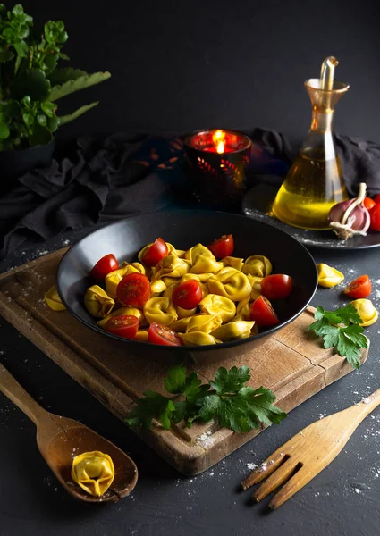 Ravioli with tomatoes on black plate in rustic homemade food environment, aerial view - image