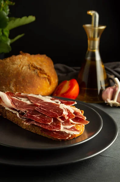 黒いプレートと素朴な背景にイベリアハムとトーストパン — ストック写真