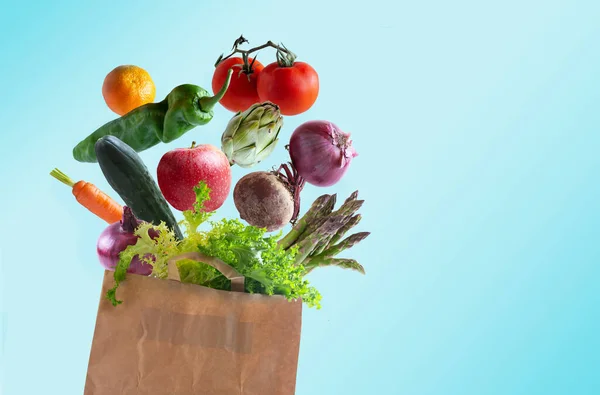Vegetables flying in recyclable paper bag with copy space, blue background