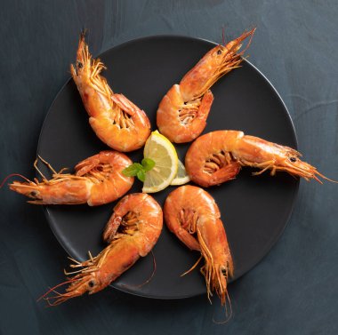 Siyah bir tabakta ızgara karidesler, ahşap bir masa, üst manzara.