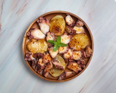 Pişmiş ahtapot yemeği dilimlenmiş haşlanmış patates, tütsülenmiş paprika ve zeytinyağıyla servis edilir. Mermer arka planda