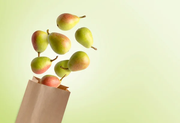 Flying pears, recyclable paper bag, green background, copy space