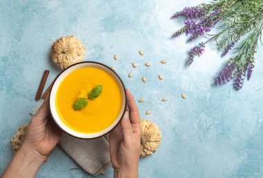 Mavi kırsal arka planda bir kase balkabağı kreması tutan eller