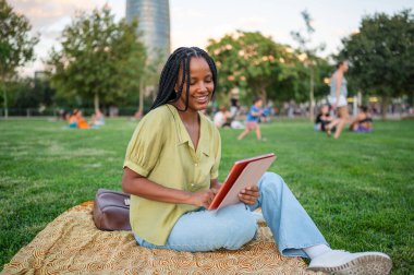Genç siyahi kadın yaz boyunca parkta tablet kullanıyor.