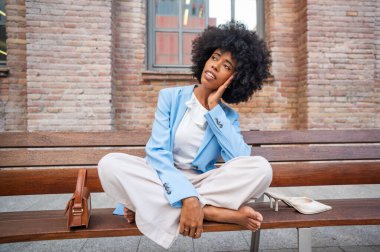 Genç yönetici uzun bir iş gününden sonra bankta dinleniyor, yüksek topuklarını çıkarıyor ve dinlenme anının tadını çıkarıyor.