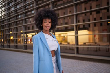 Modern ofis binasının yakınında yürüyen kendine güvenen bir iş kadını.