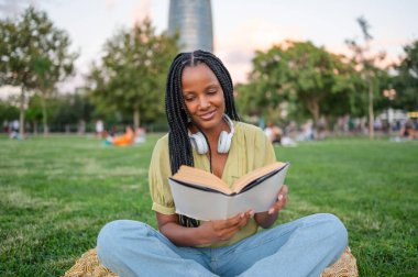 Genç siyahi kadın parkta kitap okuyor.
