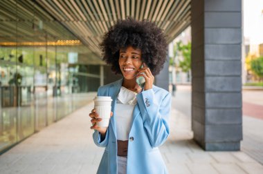Businesswoman talking on phone and holding coffee outside office building