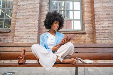 Businesswoman using tablet sitting on bench with crossed legs and barefoot