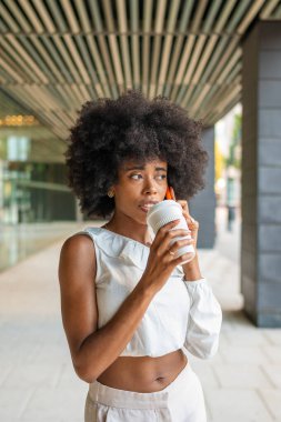 Young manager drinking a takeaway coffee and making a phone call during her coffee break