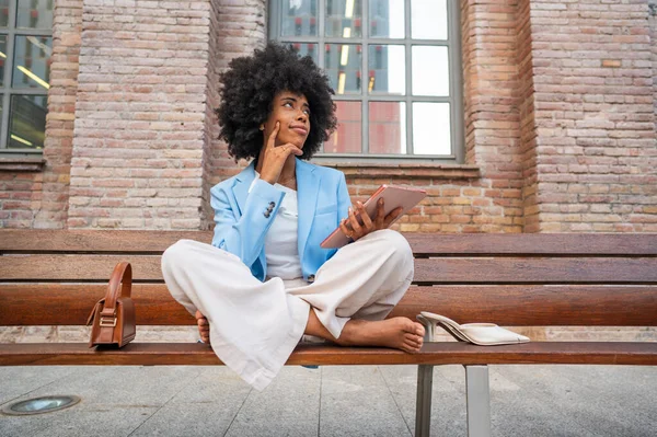 Young manager is using tablet and thinking about new ideas while sitting on bench outdoors