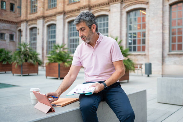 Businessman analyzing charts on a tablet while working remotely outdoors