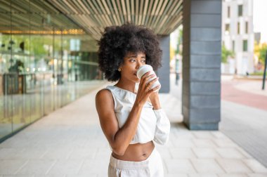 Young black woman with afro hairstyle drinking coffee from disposable cup in urban city