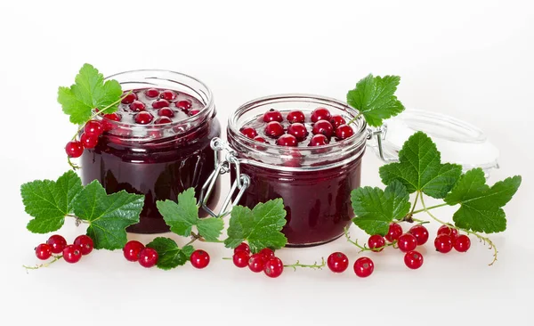 Red currant jam in jars and ripe berries with green leaves on a white background.