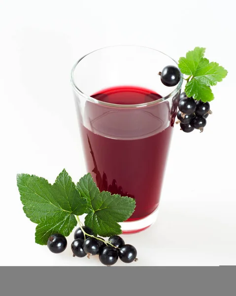 Black currant juice in a glass and ripe berries with green leaves on a white background. Top view.