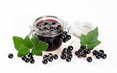 Bir kavanoz ve beyaz zemin üzerine yeşil yaprakları ile olgun meyveler siyah frenk üzümü reçeli.