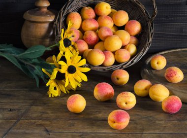 Kırmızı-sarı kayısı bir sepet ve ahşap bir masaya sarı çiçek bir buket. Karanlık fotoğraf, rustik tarzı.